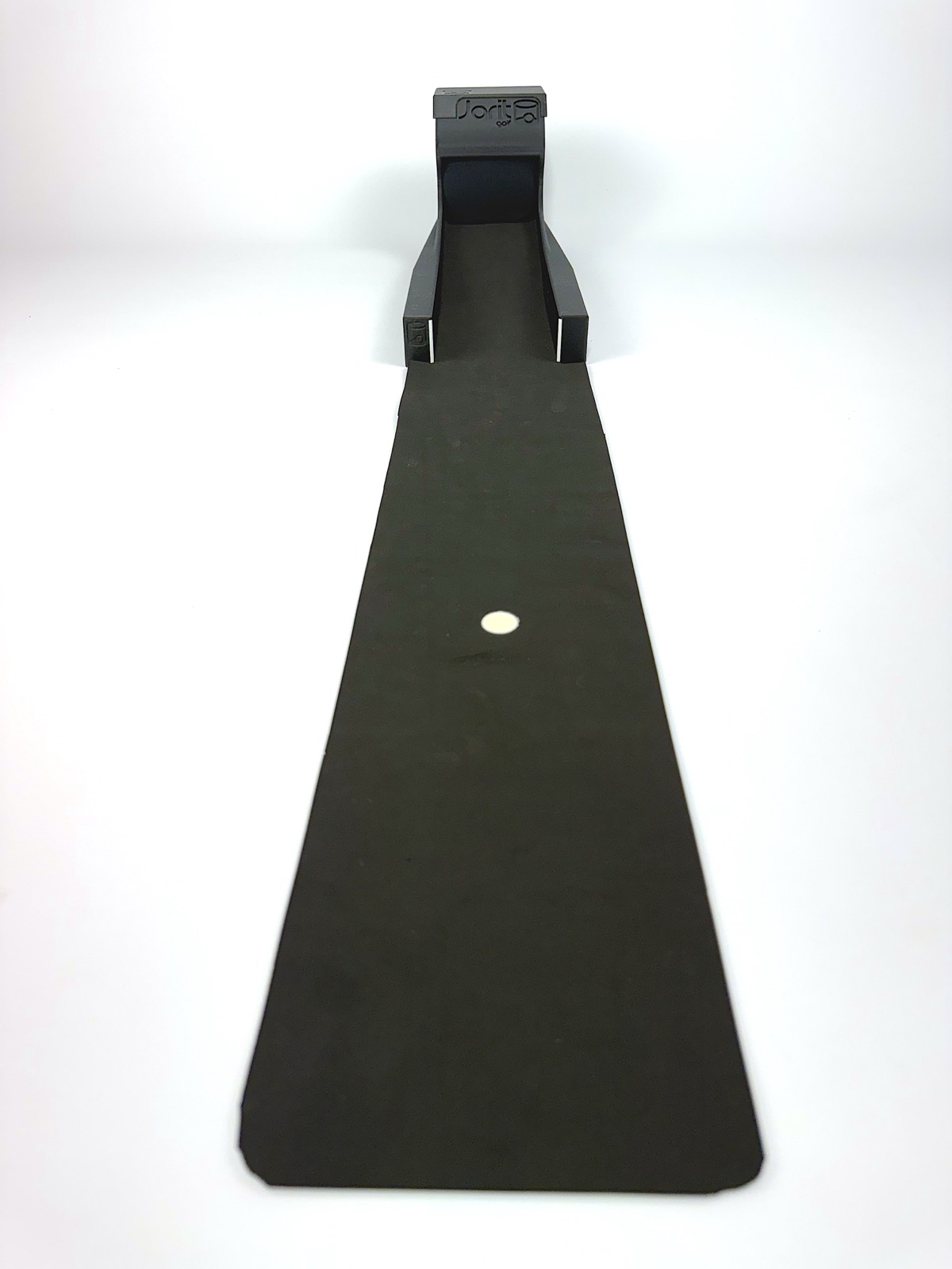 The Speed Machine head-on at the top of its black practice mat, with a golf ball waiting halfway down the roll