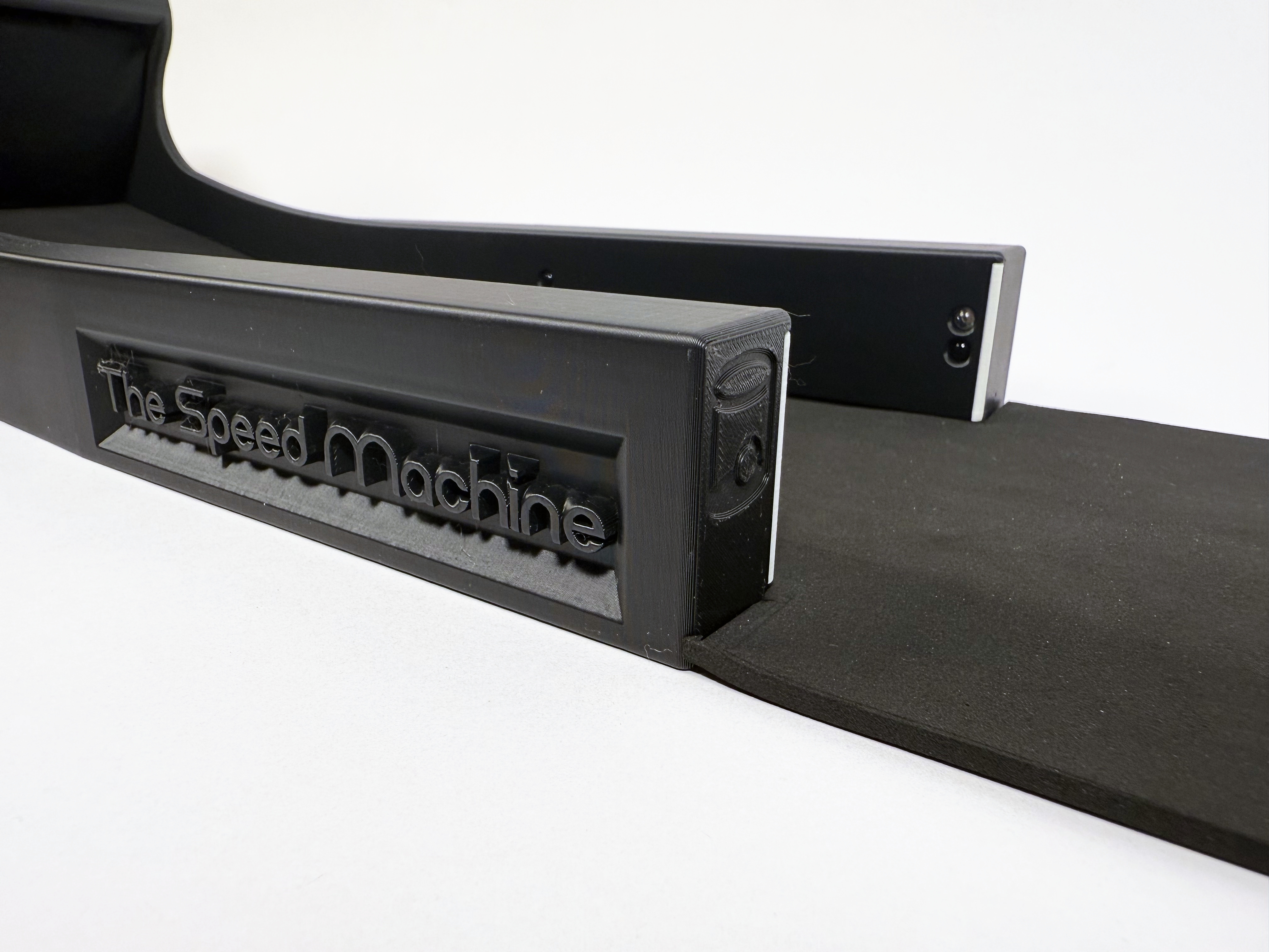 Macro of the raised The Speed Machine nameplate on the side of the return rail, the mat running off to the right